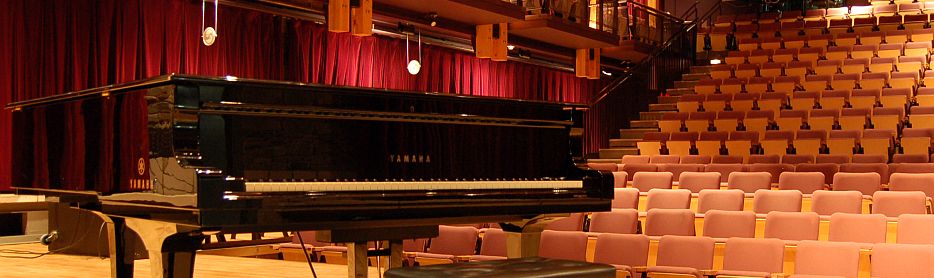 photo of piano on the Stockey Centre stage, looking out towards an empty audience of chairs